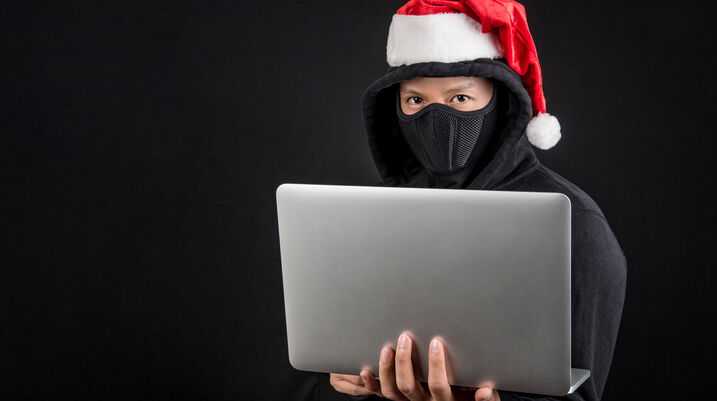 Mysterious male santa hacker holding laptop computer, anonymous man on black background, ransomware cyber attack and internet security on Christmas holiday concepts