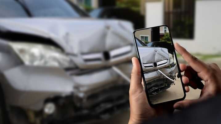 Person using smartphone to photograph front-end damage of a silver car after an accident