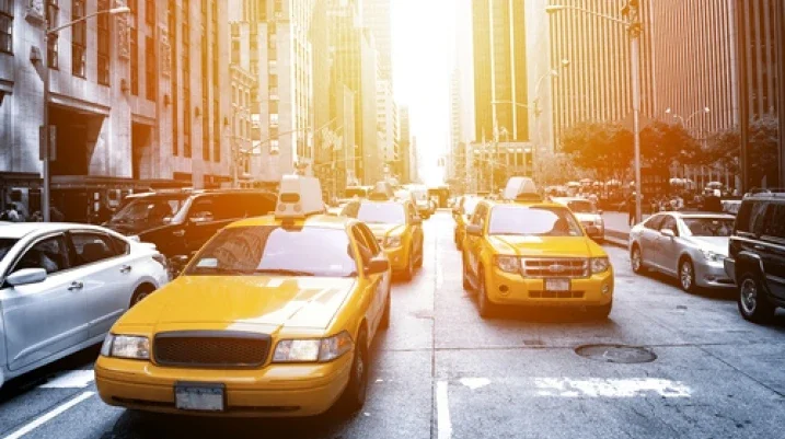 Yellow taxicabs in busy New York City traffic with sunlight flaring down the avenue