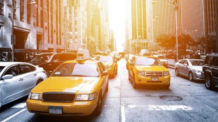 Yellow taxicabs in busy New York City traffic with sunlight flaring down the avenue
