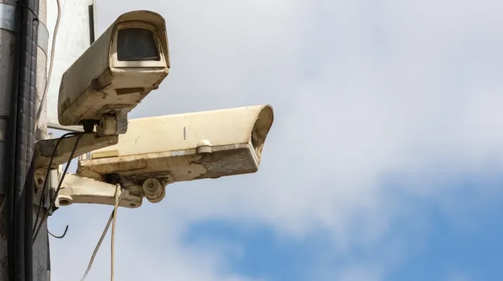 two old CCTV surveillance cameras on street pole at summer day, closeup