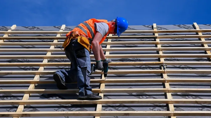 Repair and replacement of the old roof with a new one. Construction worker in protective clothing standing on roof with tools.