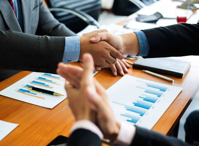 Business professionals shaking hands over a desk with financial charts, symbolizing agreement during the discovery process in legal proceedings