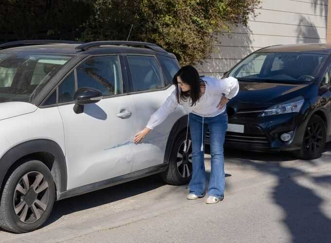 Woman inspecting scratch on white car's door in parking lot, potential car accident claim scenario.