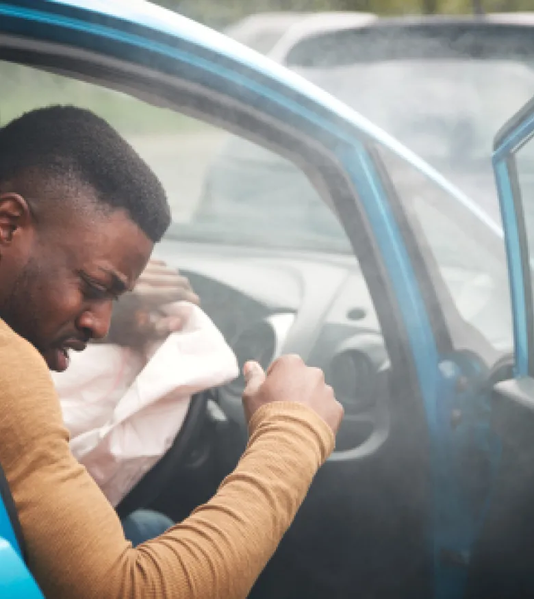  A man sits in a car, appearing injured and in pain after an airbag deployment, highlighting Airbag Injuries in Charlotte.