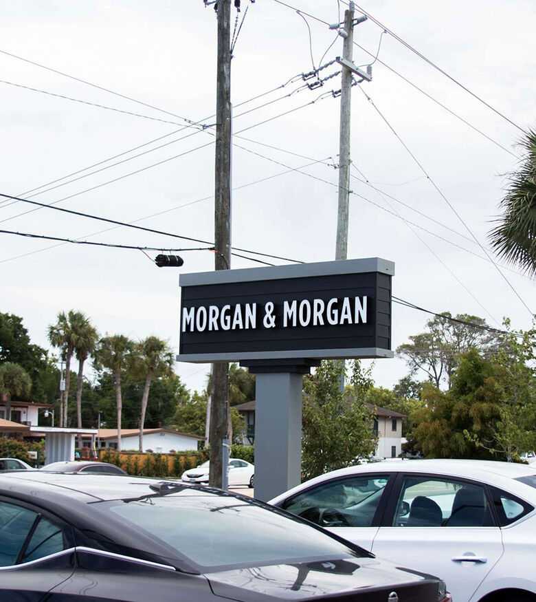 Outdoor sign of Personal Injury Lawyers in St. Augustine beside a busy road with parked cars under an overcast sky.