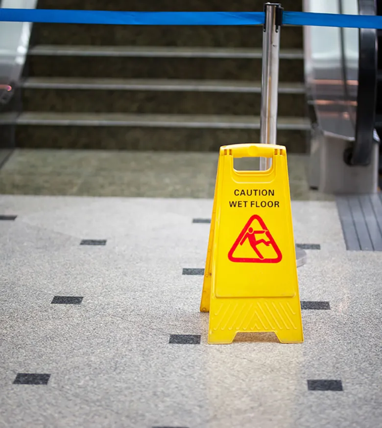 Yellow caution wet floor sign in spacious modern office with large windows and stylish furniture